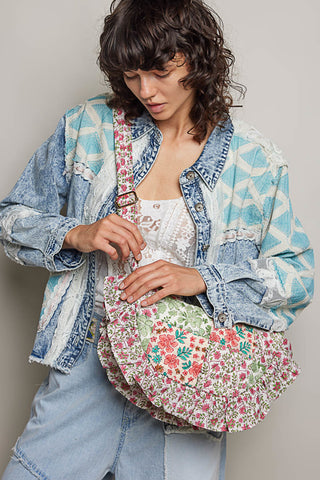 Woman holding a floral handbag wearing a patterned denim jacket against a plain background
