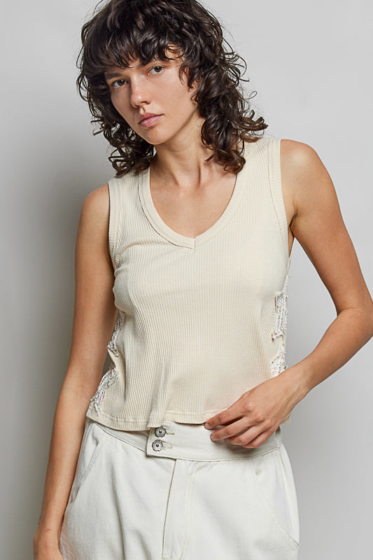 Woman wearing a beige sleeveless top with lace details against a plain background