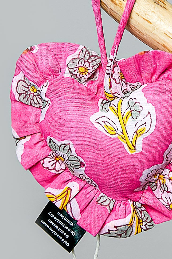 Heart-shaped pink bag charm with floral patterns and a tag on a gray background