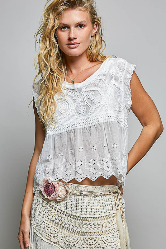 Woman wearing a white embroidered top and beige skirt against a gray background