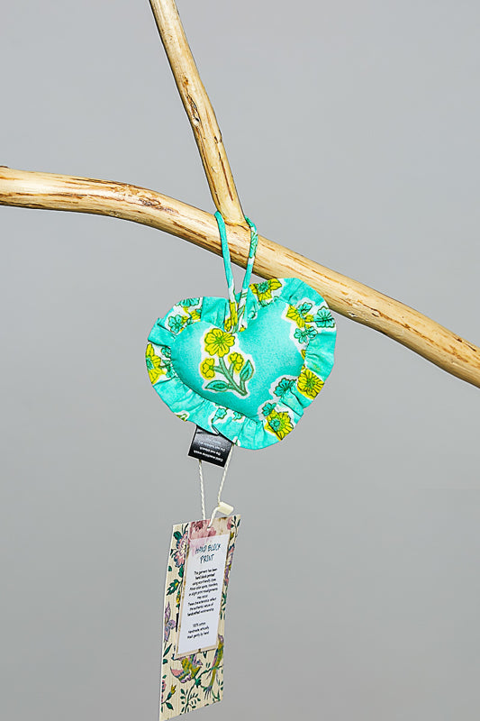 Turquoise heart-shaped fabric bag charm with floral pattern hanging on a branch against a gray background.
