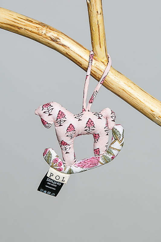 Decorative horse-shaped ornament with floral patterns hanging on a branch against a gray background.