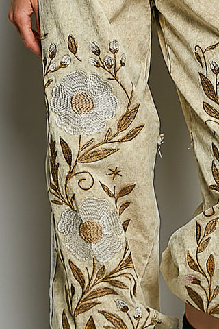 Close-up of a person's leg wearing beige wide-leg trousers with large white and brown floral embroidery.