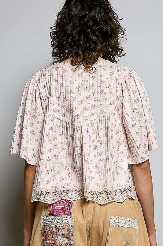 Person wearing a floral blouse with lace details on a plain background