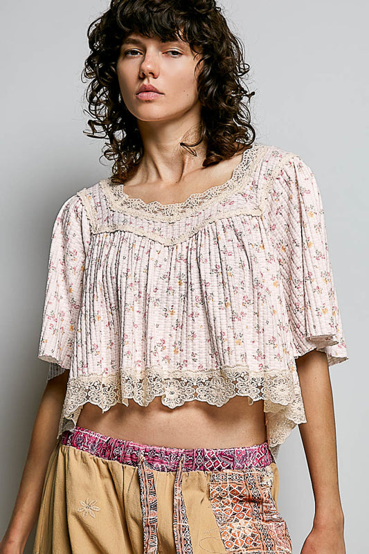 Woman wearing a floral blouse and patterned pants against a gray background