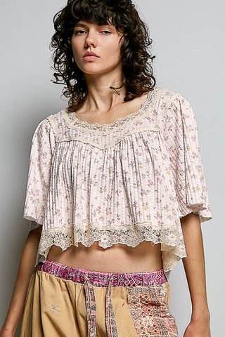 Woman wearing a floral blouse and patterned pants against a gray background