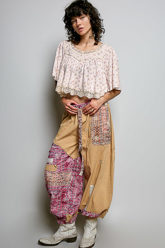 Person wearing a bohemian outfit with a floral top and beige pants on a plain background