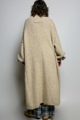 A women wearing a beige cardigan and printed pants against a neutral background.