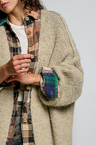 A women wearing a beige cardigan and printed pants against a neutral background.