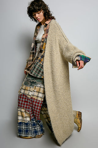 A women wearing a beige cardigan and printed pants against a neutral background.