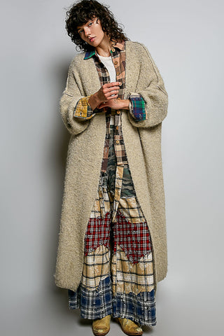 A women wearing a beige cardigan and printed pants against a neutral background.