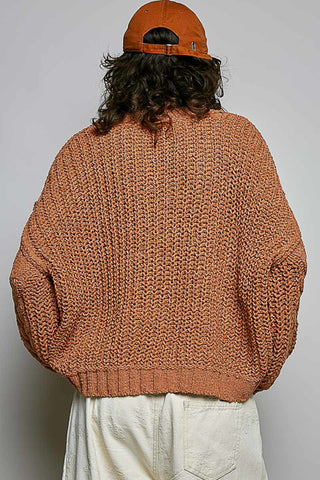 Person wearing a brown knitted sweater and orange cap from behind on a plain background