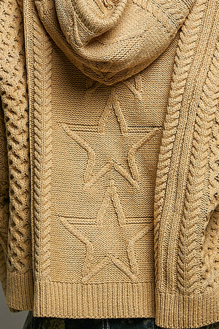 Close-up of a chunky knit cowl-neck sweater in a warm camel beige color, featuring a raised star pattern on the front and textured cable-knit borders.