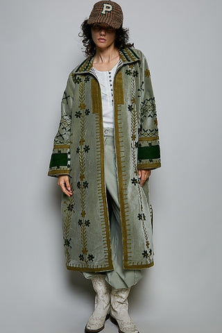 Person wearing a long patterned coat over a white outfit on a plain background