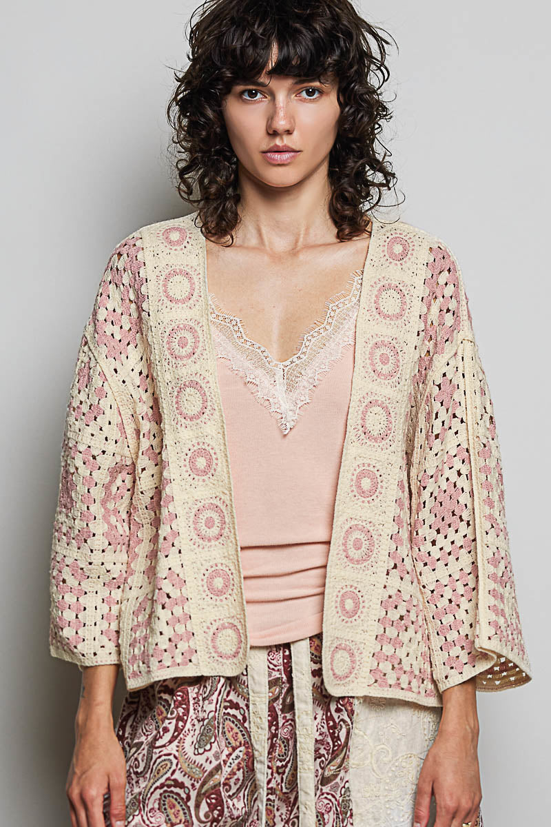 Woman wearing a patterned jacket over a pink top and paisley pants on a plain background
