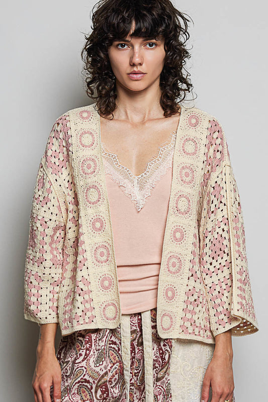 Woman wearing a patterned jacket over a pink top and paisley pants on a plain background