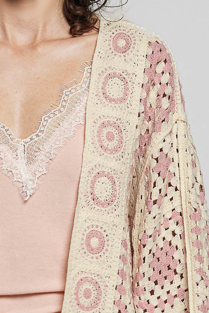 Close-up of a person wearing a pink lace top and a matching pink and white crochet shawl.