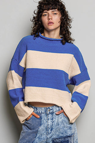 A model wearing a blue and cream striped knit sweater with a crew neck and ribbed cuffs, paired with light-wash blue jeans, against a plain gray background.
