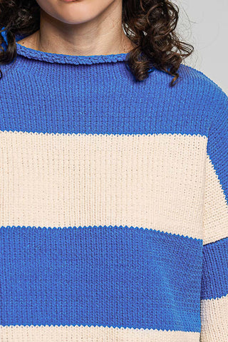 A close-up of a person wearing a chunky knit sweater with horizontal stripes in royal blue and cream.