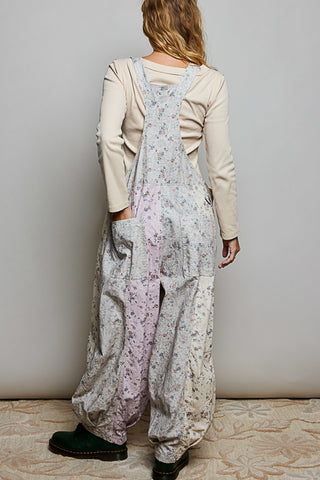 A women wearing floral printed overalls and a white top against a neutral background.