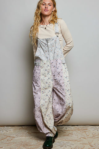 A women wearing floral printed overalls and a white top against a neutral background.