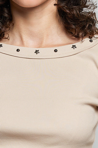 Close-up of a beige ribbed knit top with a wide boat neckline decorated with small black star-shaped studs and dark round accents.