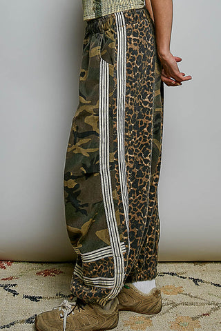 Leopard print and camouflage pants with white stripes worn by a person on a neutral background