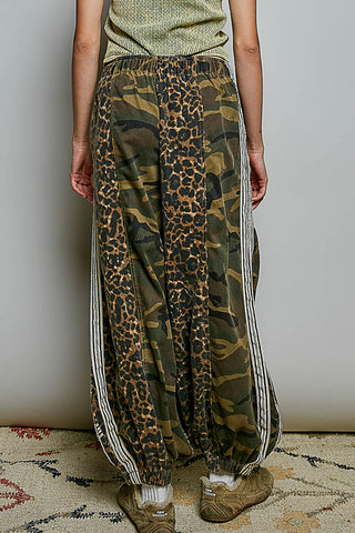 Person wearing a unique blend of camouflage and leopard print pants with white stripes on a neutral background.