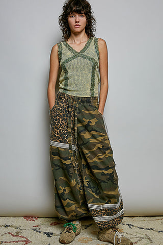 Person wearing a sleeveless green top and camouflage pants with leopard print accents on a plain background