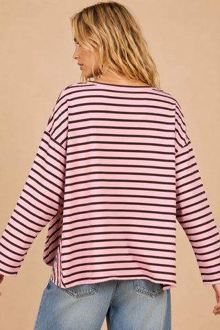 A woman shown from the back wearing a pink and black horizontally striped long-sleeve top with blue jeans, set against a solid beige background.