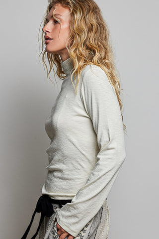 A women wearing a mock neck turtleneck against a neutral background.