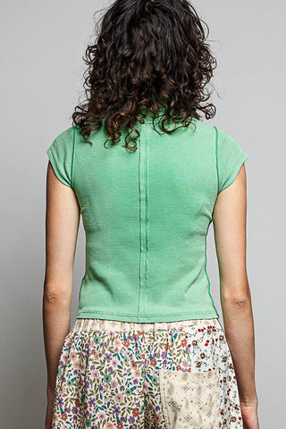 A woman viewed from behind wearing a mint green short-sleeve knit top with a center back zipper and a multicolor floral print skirt against a plain gray background.