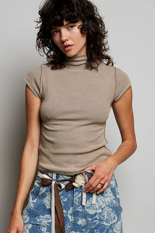 Woman wearing a beige turtleneck top and floral skirt against a plain background