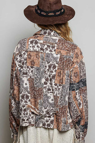 A person shown from the back wearing a brown wide-brim hat and a patchwork-print long-sleeve shirt in earthy brown, beige, and gray tones, paired with light beige bottoms, against a plain light gray background.