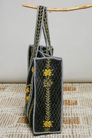 Black handbag with yellow floral embroidery hanging on a branch against a neutral background