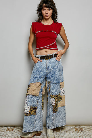 Woman wearing a red top and patchwork jeans against a plain background