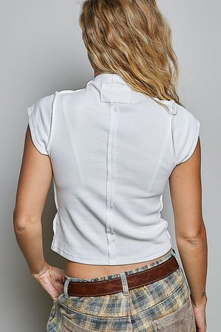 A woman shown from the back wearing a white short-sleeve crop top with a high collar and shoulder tab details, paired with a brown belt and plaid pants, against a neutral gray background.