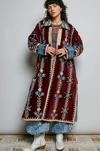 Person wearing a long patterned coat over a white outfit on a plain background