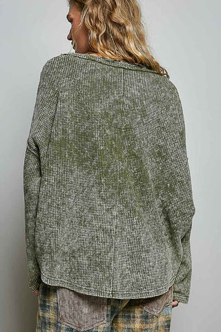 A woman shown from the back wearing a textured, long-sleeve button-up shirt in a heathered olive green and gray colorway, paired with plaid pants, against a plain light gray background.