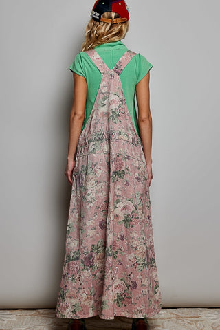 Person wearing a green shirt and floral overalls against a plain background