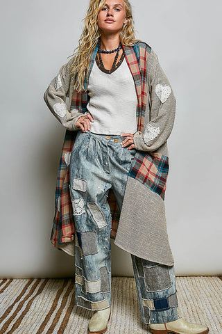 A woman models a bohemian-style outfit featuring a long gray cardigan with white heart patches and a red plaid lining, a white ribbed knit top, and wide-leg patchwork denim pants, paired with beige boots against a neutral studio background.