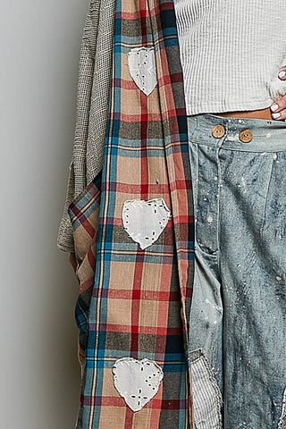A close-up of a plaid scarf with three white embroidered heart patches, styled next to a white ribbed top and distressed denim jeans.
