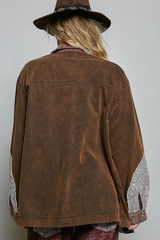 A person shown from the back wearing an oversized brown suede or corduroy jacket with contrasting light gray lace sleeve panels, a brown hat, and patterned clothing against a plain light gray background.