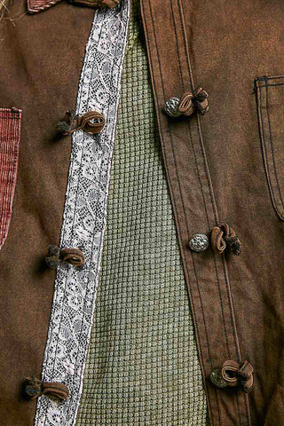 Close-up of a brown textured jacket with dark brown knotted buttons, a white lace panel, and a green patterned lining.