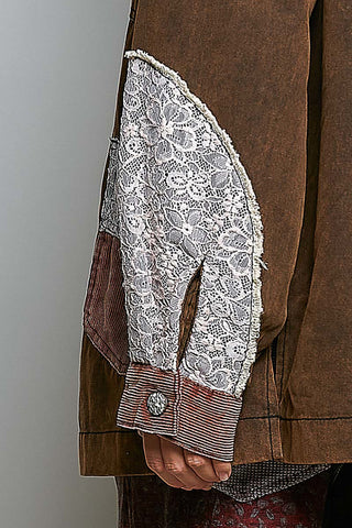 Close-up of a brown jacket with a long sleeve featuring a white floral lace panel and striped cuff, worn by a person.
