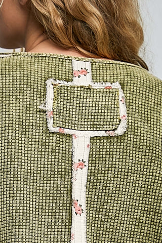 Close-up of the back of a textured olive green woven top with a cream floral embroidered patchwork detail on the back.
