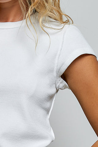 Close-up of a person wearing a white short-sleeve ribbed knit top, showing the shoulder, sleeve, and side of the torso against a light gray background.