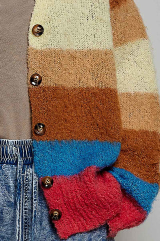 A close-up of a fuzzy knit cardigan with horizontal stripes in cream, tan, brown, blue, and red, featuring dark brown buttons, styled with blue jeans.