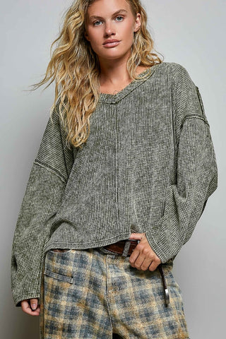 A woman modeling a loose, oversized long-sleeve knit top with a fine black-and-white micro-check pattern, paired with plaid pants, against a plain light gray studio background.