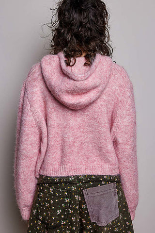 A person shown from the back wearing a fuzzy pink hooded sweater and a dark green floral skirt with a gray patch pocket, against a plain light gray background.